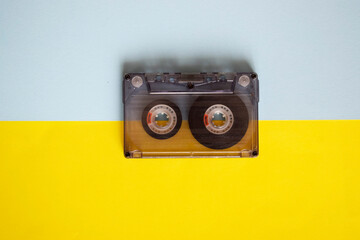 Audio cassette in the middle on a blue and yellow background, top view.