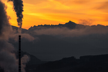 Smoking chimney and mountains with and colorful sky at background.