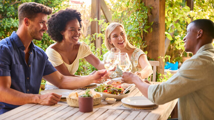 Group Of Smiling Multi-Cultural Friends Outdoors At Home Eating Meal And Drinking Wine Together