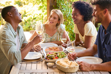 Group Of Smiling Multi-Cultural Friends Outdoors At Home Eating Meal And Drinking Wine Together