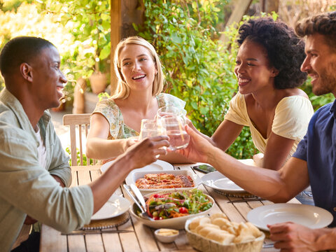 Group Of Smiling Multi-Cultural Friends Outdoors At Home Eating Meal And Making A Toast With Water