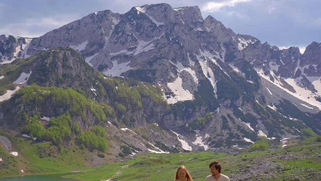 A young couple, dressed in casual clothes, takes a leisurely stroll through a lush valley with snow-capped mountains in the background. The peaceful surroundings set the tone for the couple's relaxed
