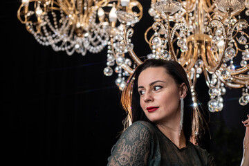 Brunette in a dark dress on the background of a chandelier