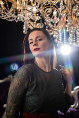 Fototapeta premium Brunette in a dark dress on the background of a chandelier