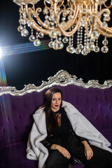 Brunette with red lipstick in a white fur coat on a purple sofa