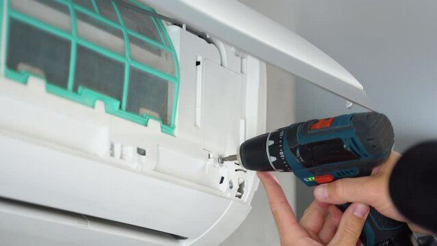 Electrician with screwdriver repairing air conditioner in apartment