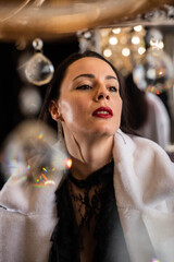 Brunette with red lipstick in a white fur coat on the background of a chandelier