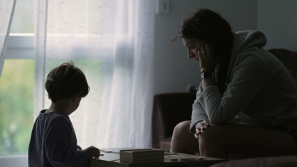 Candid mother and child playing board game at home in silhouette by window curtains. Parent and kid bonding. Childhood education lifestyle