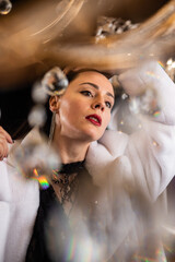 Brunette with red lipstick in a white fur coat on the background of a chandelier