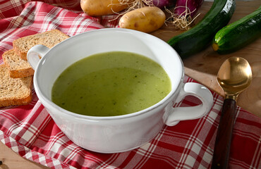 Zucchini soup in a white bowl on a wooden table with ingredients around