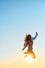 Playful woman jumping against sky at sunset and looking at camera.