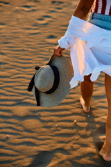 Close up of woman carrying straw hat while walking down the beach.