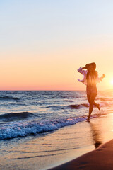 Young cheerful woman running through sea at sunset.