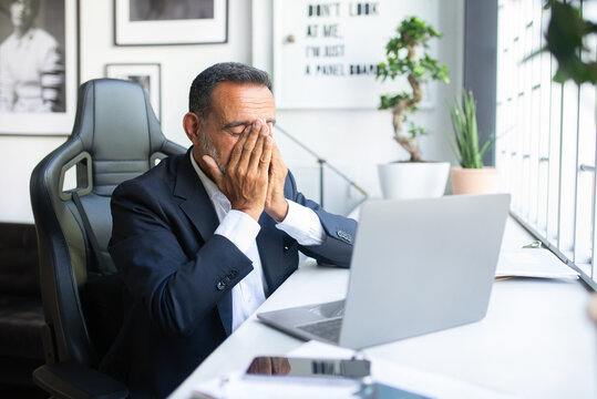 Tired sad old caucasian man in suit resting with laptop at table, suffer from problems, migraine