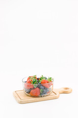 immagine primo piano di ciotola in vetro con frutti di bosco freschi da filiera biologica, fragole e mirtilli, tagliere in legno superficie bianca