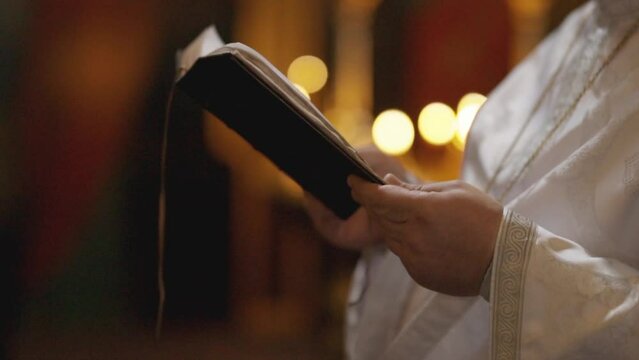 An Orthodox priest holds a Bible in his hands. Close-up of unrecognizable hands of a priest holding a bible in a church. A priest with a Bible. Christianity or Catholicism, faith in God. Church ritual