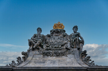 Copenhagen, Denmark - September 14, 2010: Closeup of blackened marble monumental gate tower top featuring golden crown and 2 male figures against blue sky
