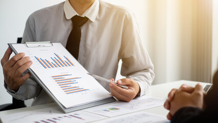 Two business people sitting at workplace and discussing about earnings on a graph to plan investments.