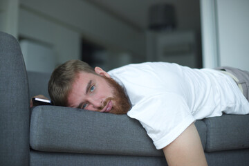 Young bearded man sleep at home on couch with his cell mobile phone in living room. Smartphone...