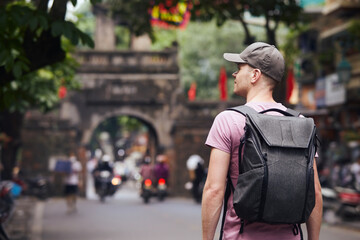 Traveler walking on busy asian street. Rear view of man with backpack in Old Quarter in Hanoi,...