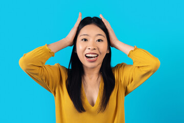 Emotional asian woman gesturing on blue, showing amazement