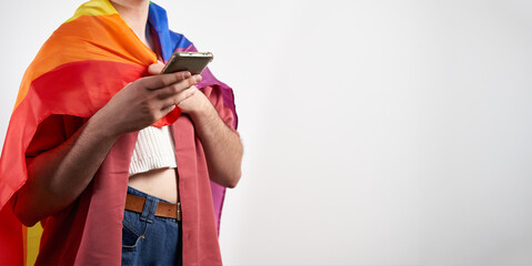 Non-binary person texting with smartphone with lgbt rainbow flag as cape on pride month over white background with copy space