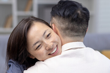 Close-up photo. Young Asian couple, family hugging together. Happy face of young woman hugging and supporting her husband, meets smiling at home.