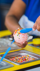 Decorating a strawberry ice cream cone with colored sprinkles