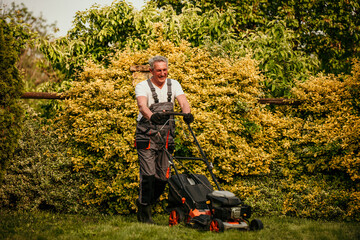 Senior gardener trimming grass with lawn mower