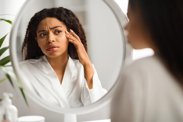 Worried Black Woman Looking In Mirror And Touching Wrinkles On Her Face