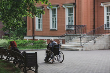 Obraz premium An elderly man in a wheelchair walks in the park outdoors. Disability. Health problems. Medicine, life insurance and healthcare.