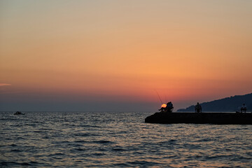 Sea pier at sunset, where fishermen are fishing
