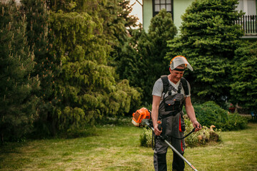 Senior caucasian man farmer gardener standing in the field with a string trimmer