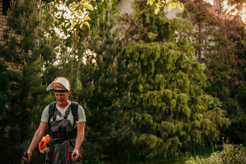 Obraz premium Senior caucasian man farmer gardener standing in the field with a string trimmer
