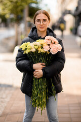 Fototapeta premium Young beautiful woman with large bouquet of yellow, pink, lemon and milk colors carnations in hands.