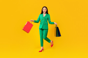 Full length shot of excited woman walking with bright shopping bags, enjoying successful seasonal sales