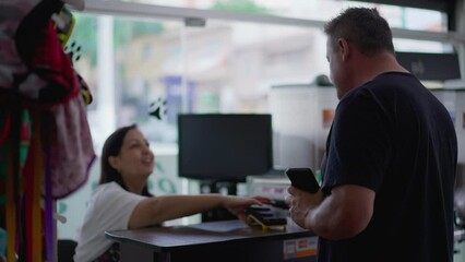 Male customer paying with phone at small business counter with joyful female entrepreneur of Pet Shop. Contactless mobile payment