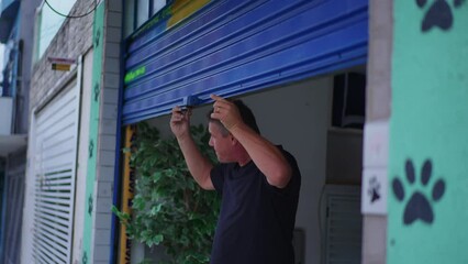 Man opening storefront garage in city sidewalk. Person slides business shop in street