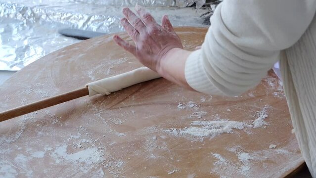 Women's hands roll out the dough in a thin layer on a wooden board, cooking the national dish of Turkey.