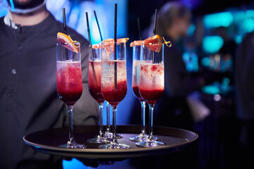 The waiter holds several glasses of champagne-based cocktails with grapefruit slices on the glasses