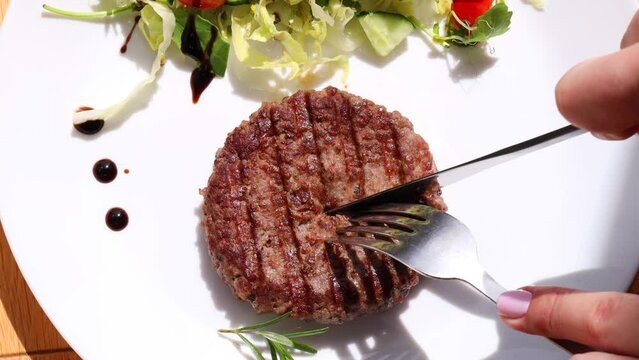 Beef cutlet grill with stripes outdoors and fresh salad on a white plate. dinner. Girl cuts a cutlet with a knife
