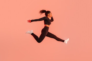 Fototapeta na wymiar Athlete black woman in sportswear jumping and having workout on red neon studio background, copy space, full length