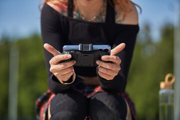 Gamer girl playing online video games on a mobile phone. Young female person plays a mobile game on a smartphone outdoor