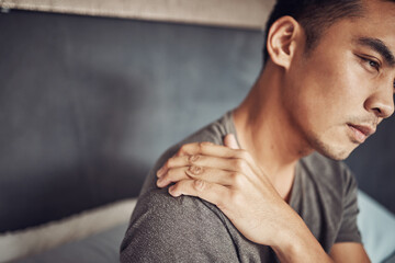 Stress, sick and man with shoulder pain in his bedroom in recovery from an accident or injury. Illness, medical emergency and male person holding a sprain back muscle while resting in his apartment.