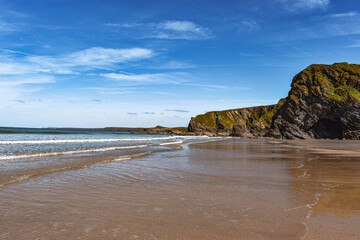 Tide coming in on golden sand with blue skies and coastline in distance