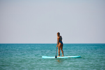 Happy female surfer enjoys in standup paddleboarding at sea.
