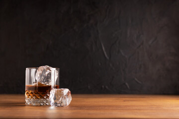 Whiskey or rum with an ice cube on a wooden table with a black background