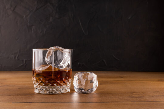 Whiskey or rum with an ice cube on a wooden table with a black background