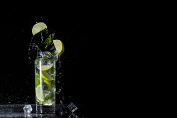 Cold mojito cocktail with mint lime and ice on a black background with splashes and falling ice