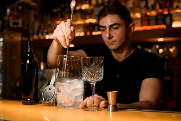 Barman holds long spoon and spreads out pieces of ice in mixing cup